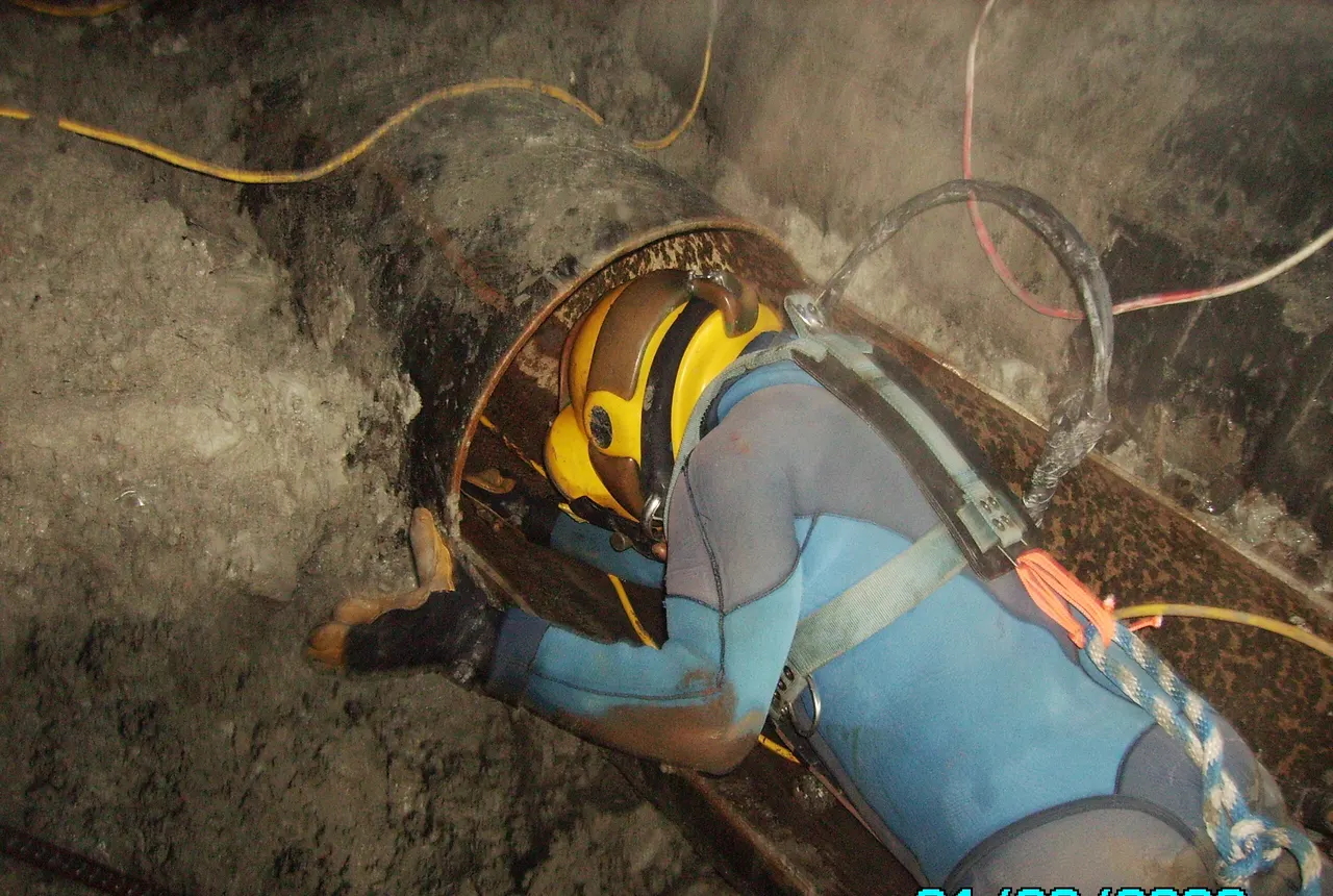 Commercial diver in a Kirby Morgan helmet working inside a flooded pipe