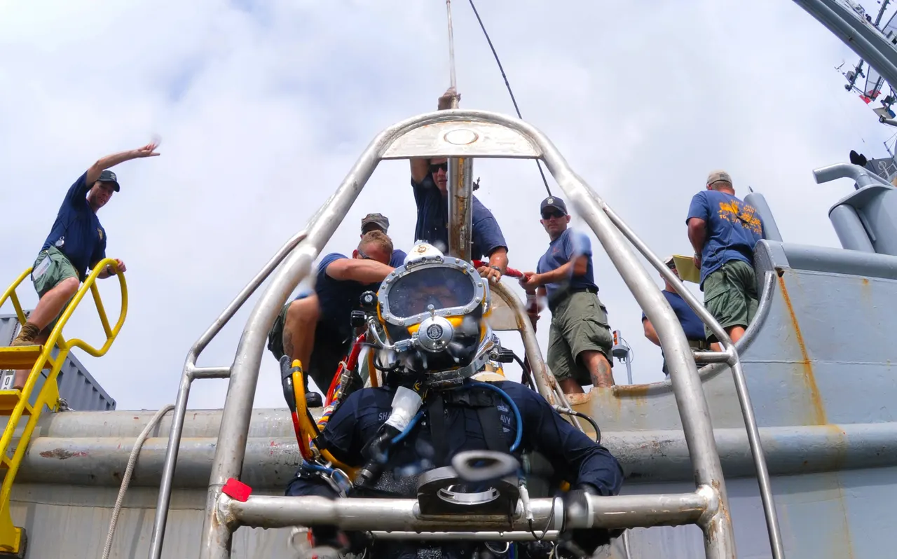 Diver on a dive stage being prepared by tenders on a ship deck